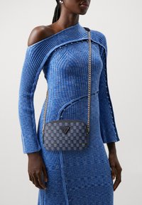 Blå ribbet kjole med off-shoulder design og knapdetaljer, parret med en mønstret, rektangulær taske med kædetræk og logo-detalje.