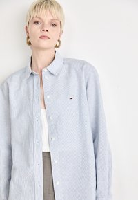Camicia button-up azzurro chiaro realizzata in tessuto a righe, con colletto a punta e un piccolo logo sul petto. Tessuto morbido e vestibilità rilassata.