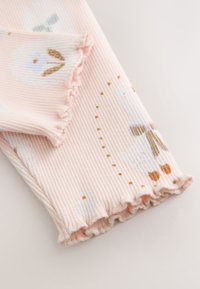 Rosa gerippte Leggings mit weißen und pastellfarbenen Blumenmustern, Rüschensäumen und goldenen Punktakzenten für zusätzliche Details.