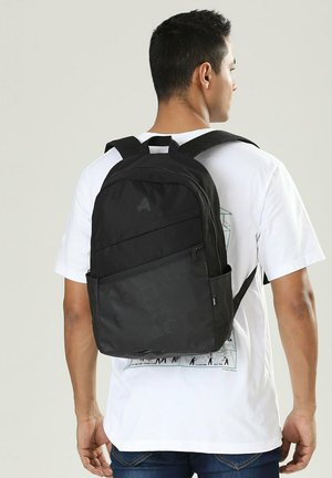 Zaino nero realizzato in materiale resistente, dotato di spallacci imbottiti, una tasca frontale con zip e una tasca laterale in rete per bottiglie d'acqua.