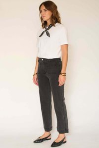 Jean en denim noir taille haute avec jambes droites, poches avant et arrière ; porté avec un t-shirt blanc et une écharpe noire à motifs.