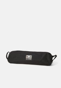 Zwarte tas met rits en twee zijhandvatten, met een logo patch. Het materiaal lijkt duurzaam, met een gladde, matte textuur.