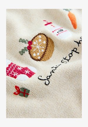 Coperta lavorata a maglia con tessuto color crema, decorata con ricami di calze di Natale, una torta, una bottiglia di latte e un regalo incartato.