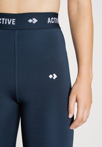 Granatowe legginsy sportowe z szerokim paskiem, na którym widnieje napis "ACTIVE" w białym kolorze, z małym białym logo z przodu.