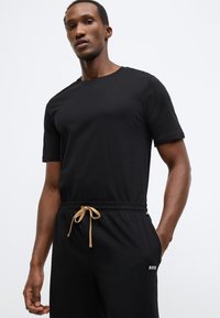 Μαύρο κοντομάνικο t-shirt από βαμβακερό ύφασμα, συνδυασμένο με ελαστικό μαύρο παντελόνι που διαθέτει μπεζ κορδόνι και λευκό λογότυπο "BOSS".