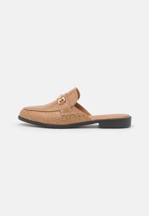 Beżowe mokasyny typu slip-on z fakturą krokodyla, złotą klamrą na cholewce, czarnym niskim obcasem i odkrytą piętą dla łatwego użytkowania.