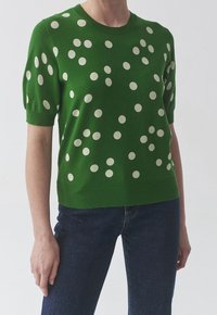 Zelený krátký svetr s kulatým výstřihem, zdobený krémovými puntíky a měkkou texturou. Kombinován s tmavými džínami z denimu.