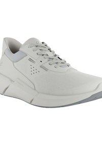 Basket de sport gris clair avec une tige en textile respirant, fermeture à lacets, semelle rembourrée et un branding subtil. Présente des détails perforés.