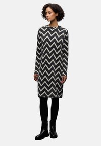 Černobílé šaty pletené ve vzoru šipky, s dlouhými rukávy, kulatým výstřihem, rovným střihem a měkkou texturou, doplněné černými kotníkovými botami.