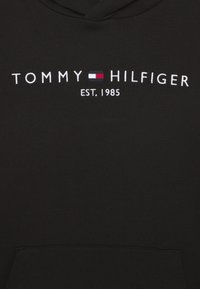 Felpa nera con cappuccio con la scritta bianca "Tommy Hilfiger", un piccolo logo della bandiera rosso, bianco e blu, e "EST. 1985" ricamato sul davanti.