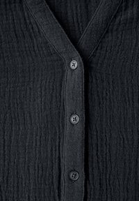 Sort tekstureret cardigan med V-hals og fem sorte knapper fortil. Stoffet har et krøllet mønster for ekstra dimension.