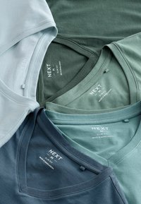Patru tricouri cu guler în v formă, în nuanțe variate: albastru deschis, verde, verde închis și bleumarin. Fiecare are un design slab și eticheta brandului.