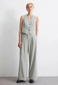 Gilet sans manches gris à rayures fines avec trois boutons, associé à un pantalon large ; texture lisse, coupe ajustée, design minimaliste.