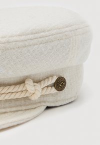 Off-white textured fabric cap with twisted rope detail and a round metal button engraved with "Brixton."