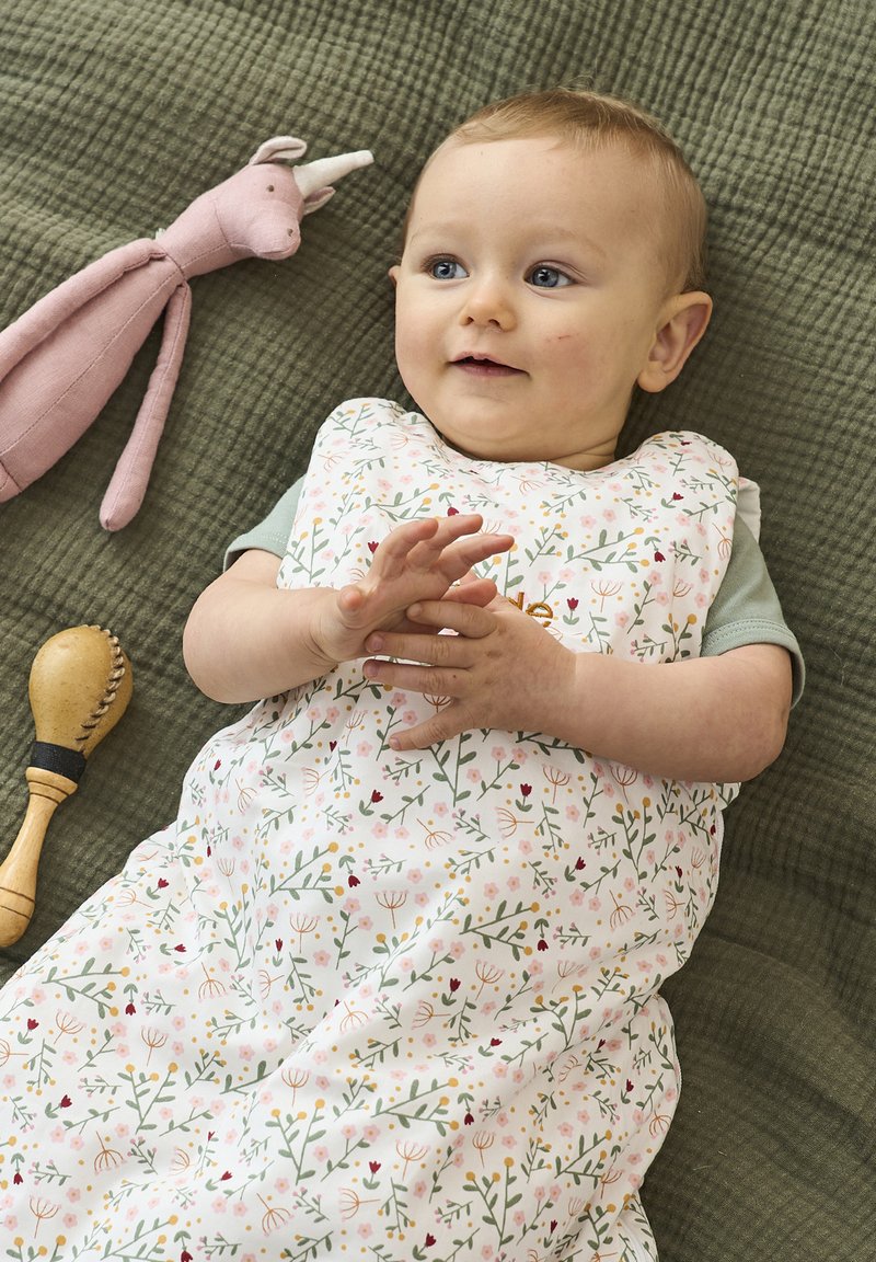 Floral sleeping bag featuring pink, green, and yellow patterns on a white background, with a soft texture, displayed on a quilted green surface.