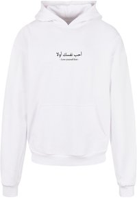 Hvit hettegenser laget av bomullsblanding med en frontlomme. Har arabisk tekst og engelsk setning, "Elsk deg selv først," i svart.