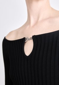 Black ribbed top featuring an off-shoulder design with a keyhole neckline. Detailing includes a silver hardware accent at the opening.