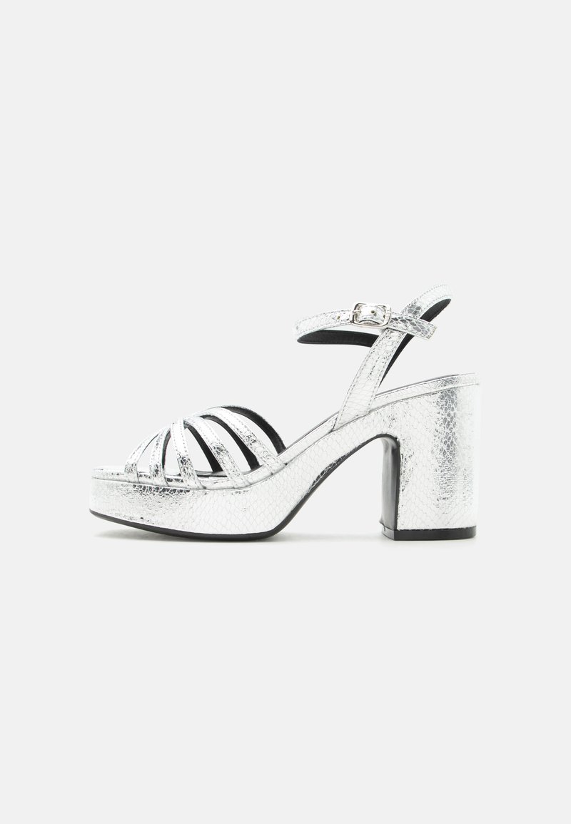 Ασημί μεταλλικό πέδιλο με ψηλό τακούνι, αγκράφα στον αστράγαλο, πολλαπλά λωρίδες μπροστά, χοντρό τακούνι και διακριτό υφασμάτινο σχέδιο στην επιφάνεια.