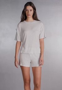 Světlé šedé bavlněné domácí oblečení sestávající z volně střiženého trička s krátkým rukávem a odpovídajících šortek, s hladkou strukturou a jednoduchým designem.