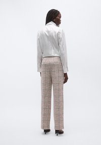 Light gray, glossy, cropped jacket with a high collar; paired with high-waisted, patterned, wide-leg trousers in muted tones.