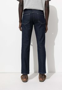 Jean en denim de lavage foncé, design à jambe droite. Comprend deux poches arrière, un minimum de couture et un léger effet usé au niveau de l'ourlet. Porté avec des sandales.