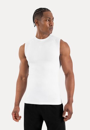 Homme musclé avec des cheveux tressés portant un débardeur blanc de sport et un short noir, regardant sur le côté devant un fond uni.