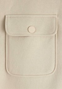 Tascherina in tessuto beige con una patella arrotondata e chiusura centrale a bottone, caratterizzata da cuciture lungo i bordi per un tocco di dettaglio e durata.