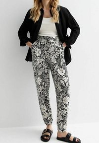 Mustat ja valkoiset kukkakuosiset housut, joissa on joustava vyötärö, kuminauhakäändöt nilkoissa ja sivutaskut, yhdistettynä mustaan paitaan ja sandaaleihin.