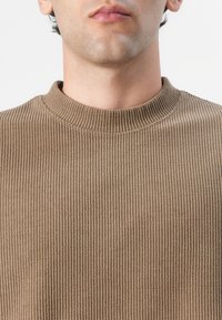 Maglione marrone a coste con un collo a girocollo alto, tessuto testurizzato e design aderente, che presenta una tonalità calda e tenue.