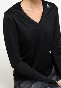 Černé sportovní tričko s dlouhým rukávem a výstřihem do V, vyrobené z hladkého, pružného materiálu. Obsahuje malé logo Reebok na levém rameni.