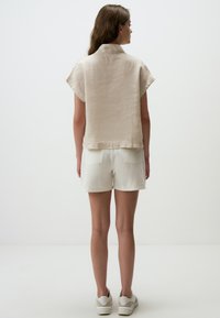 Beige linnen T-shirt met korte mouwen en kraag, met een textuurafwerking en een iets losse pasvorm, gecombineerd met witte shorts en lichte sportschoenen.