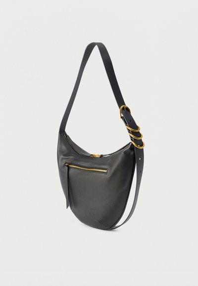Μαύρη δερμάτινη τσάντα ώμου με χρυσλό φερμουάρ και διακοσμητικούς χρυσούς κρίκους σε ρυθμιζόμενο λουράκι, σε απλό φωτεινό φόντο.