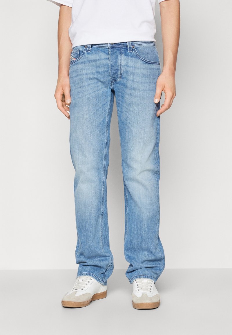 Jeans en denim bleu clair avec une coupe droite, dotés de poches latérales et d'un léger décoloré. Portés avec des baskets blanches.