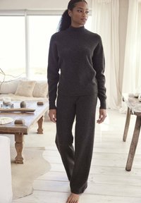 Dunkelgrauer, gestrickter Pullover mit hohem Kragen und langen Ärmeln, kombiniert mit passenden, locker sitzenden Hosen. Weiche Textur vor hellem Hintergrund.