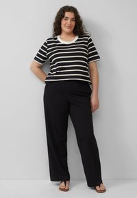Zwart-wit gestreepte T-shirt met een ronde hals en korte mouwen, gecombineerd met zwarte wijde broek en slippers.