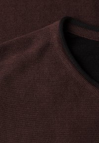 Gros plan d'un tissu brun foncé texturé avec un col plié montrant une doublure intérieure noire et des détails de couture fins.