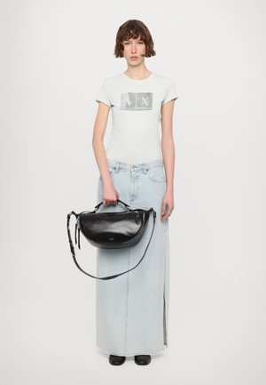 Sac en cuir noir avec une forme incurvée, tenu à la main. Porté avec un t-shirt bleu clair arborant un graphique argenté et une jupe en denim.