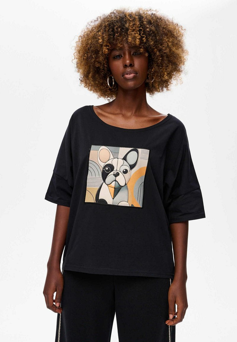 Black t-shirt with loose fit and wide neckline featuring a colorful geometric dog print on the front. Short sleeves and soft fabric texture.