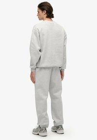 Grå sæt med sweatshirt og sweatpants lavet af blødt bomuldsblanding. Har ribbede manchetter og kant, med minimal branding på bagsiden.