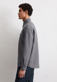 Camicia a maniche lunghe grigia in tessuto leggero con colletto abbottonato, taschino sul petto e dettagli con bottoni sulle maniche.