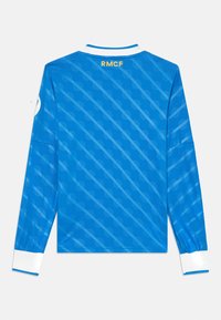 Langermet sportsjersey i lys blått stoff, med et kjedemønster, hvit krage og "RMCF"-tekst i gult på baksiden.