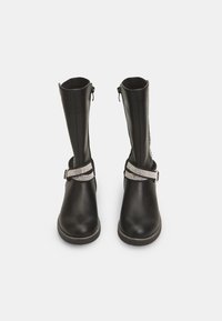 Botas negras hasta la rodilla hechas de material sintético suave. Cuentan con una correa adornada con strass plateados alrededor del tobillo y cremalleras laterales.