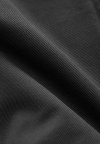 Tejido ribeteado negro con una textura suave, que muestra pliegues y contornos. La superficie refleja la luz sutilmente, enfatizando el patrón de ribete.