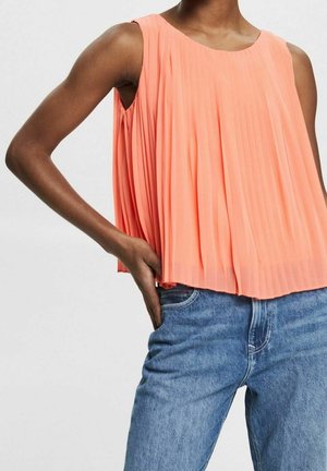 Ferskenfarvet plisseret ærmeløs top med rund halsudskæring. Stoffet er let og har en blød tekstur. Kombineret med blå cowboybukser.