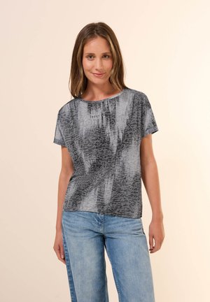Un haut gris à manches courtes avec un motif texturé présentant différentes nuances de gris et un design de texte imprimé sur le devant. Associé à un jean bleu.