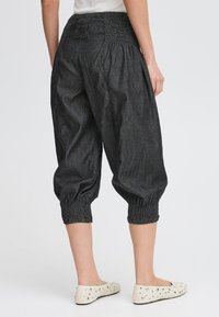 Pantalons en denim foncé, cropped, avec une taille smockée, des jambes fuselées et des poignets élastiques. Assortis à des chaussures plates de couleur claire.