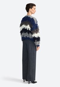 Sudadera de pullover con diseño de flecos en azul marino, gris, blanco y negro, combinada con pantalones de pierna ancha grises y zapatos de tacón negros.