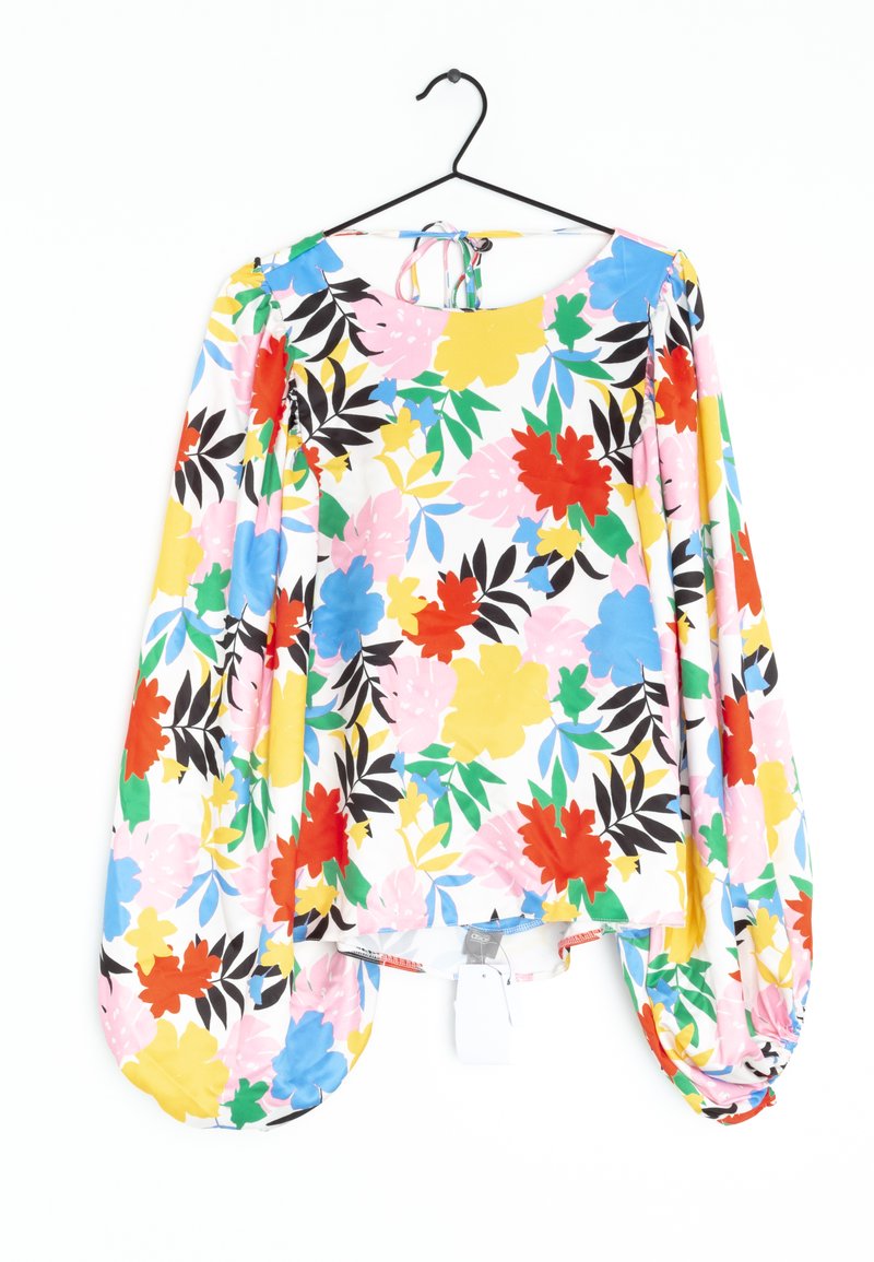 Blouse florale avec un fond blanc, des fleurs colorées en rouge, jaune, bleu et rose, avec des manches bouffantes et un col à nouer dans le dos.