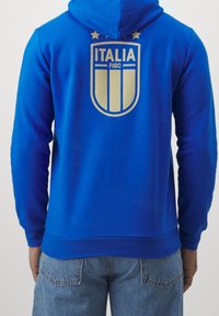 Królestwo niebieska bluza z kapturem z złotym napisem "ITALIA" oraz herbem FIGC z tyłu, z dwoma złotymi gwiazdami nad emblematem i kieszenią kangurzą.