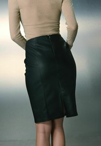 Jupe crayon en cuir noir avec une fente au dos, présentant une texture lisse et une coupe ajustée, associée à un haut beige à manches longues.